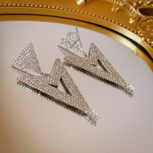 Macro shot of silver-tone triangle earrings with zircons reflecting on a mirror