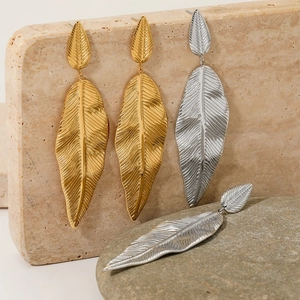 Artistic display of layered leaf-shaped earrings in gold and silver on natural stones