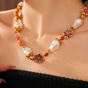 Detail of vintage gold necklace with baroque pearls and red floral gems on model