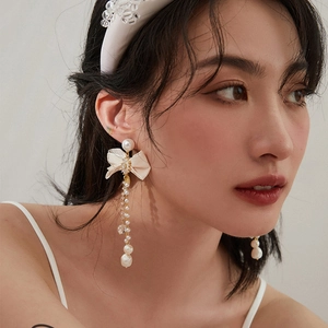 Elegant asymmetrical bow pearl tassel earrings worn by a model in a professional setting