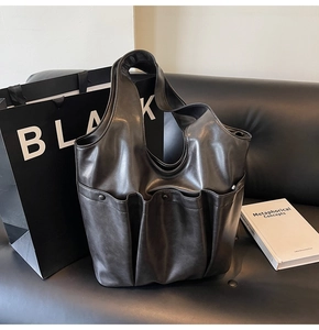 Detail of black faux leather tote bag with multi-pocket design on a leather sofa