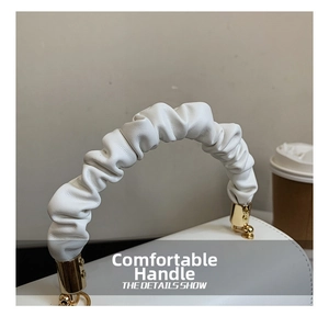 Close-up of ruched handle detail on white leather handbag with golden metal hardware