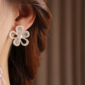 Gros plan d'une boucle d'oreille fleur en argent avec perle et pétales en maille ajourée
