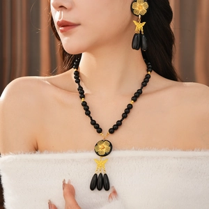 Elegant model wearing black beaded necklace set with gold flower and butterfly pendants