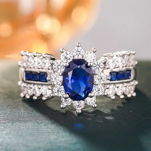 Makroaufnahme eines blauen Saphirrings mit diamantbesetztem Heiligenschein auf grünem Grund