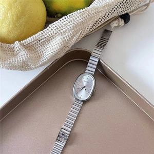 Detail view of oval silver quartz watch and chain bracelet set on golden tray
