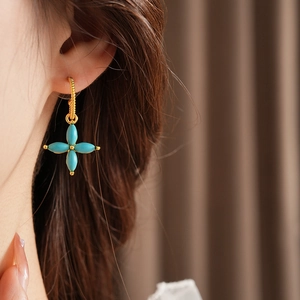 Close-up of golden four-leaf clover earrings with turquoise stone inlay on model