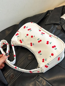Detail of white nylon underarm bag featuring red cherry prints on a black jacket