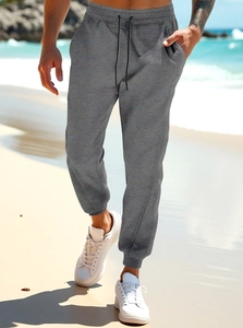 Detail of grey joggers featuring drawstring waist and ribbed cuffs on an outdoor beach