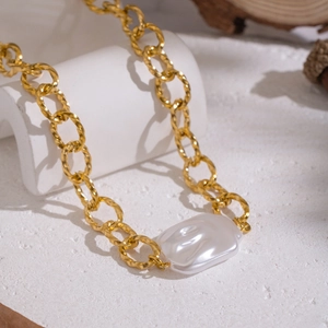 Détail d'un collier à grosse chaîne dorée avec perle baroque sur fond blanc élégant