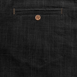 Detail of dark linen beach shirt showing a brown wooden button and reinforced pocket texture