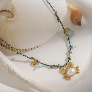 Detail der goldenen Webhalskette mit Krabbenanhänger, blauen Perlen und weißen Perlen