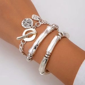 Silver metal bracelet set with heart and coin pendants on model's wrist, vintage style