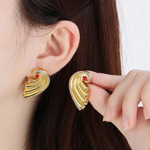 Close-up of golden wing earrings with red gemstone and white crystal accents on ear