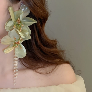 Detail of oversized green fabric flower earring with beaded tassels on female model