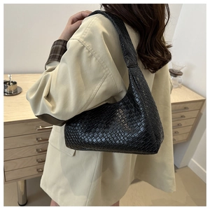 Side view of black woven shoulder bag worn with a beige coat for a stylish look