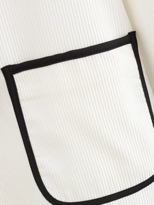 Detail of white ribbed knit fabric with contrast black piping on pocket and seam edges