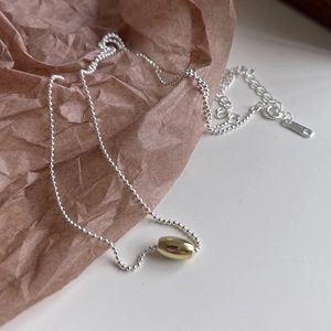 Detail of 925 sterling silver olive bead necklace with a gold accent bead on paper