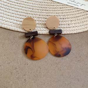 Dettaglio di orecchini boho in legno rotondo e resina ambrata su uno sfondo di carta vintage
