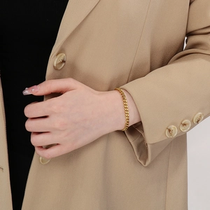 Gros plan d'un bracelet gourmette doré porté par un mannequin sur un costume beige