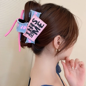 Detail of denim bow hair claw clip with pink woven rope and THIS IS ME textile label
