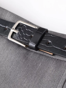Detail eines schwarzen Kroko-Ledergürtels mit silberner Schnalle an grauer Falten-Shorts