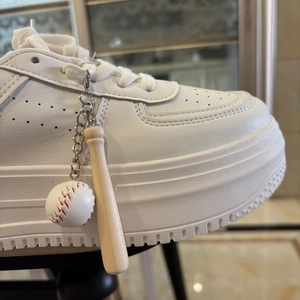 Detail of a white chunky platform sneaker featuring a mini baseball bat and ball keychain charm