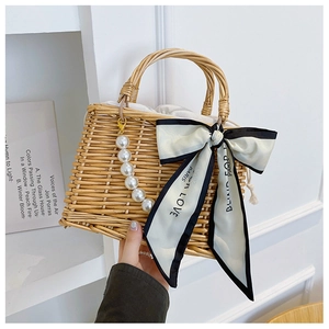 Detail of woven straw bag with pearl charm, silk bow, and drawstring lining for beach travel