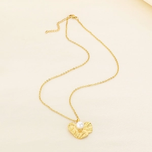 Detail of irregular textured heart pendant with white pearl on golden chain necklace