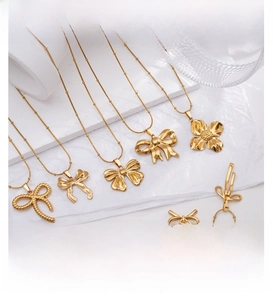 Close-up of golden bow and flower pendants on thin bead chains over a white background