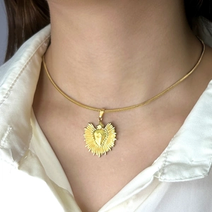 Gros plan d'un pendentif cœur doré brillant sur une chaîne serpent porté par un mannequin