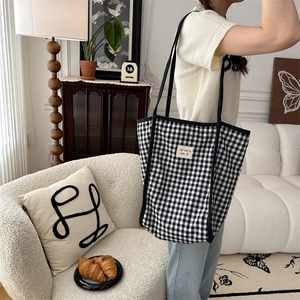 Detail of a black and white checkered canvas tote bag worn by a model in a cozy home setting