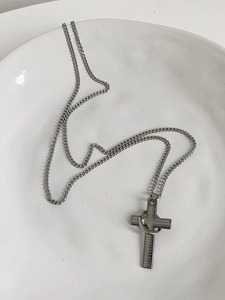 Detail view of a stainless steel cross necklace with engraved prayer and ring on a plate.