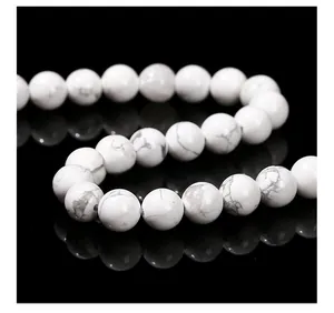 Macro view of white howlite beads with gray marble texture on reflective black background