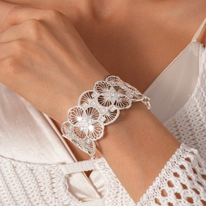 Close-up of a silver-toned openwork floral cuff bracelet worn with a satin outfit