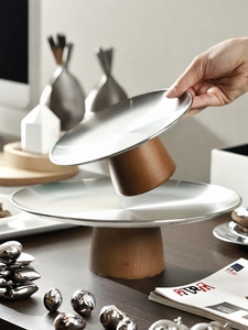 Detail of hand holding a brushed metal tray with a minimalist cylindrical wooden base