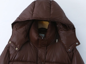 Dettaglio del parka marrone lucido con cappuccio, cerniera e bottone a pressione in metallo