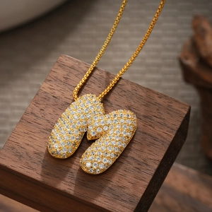 Detail of 18K gold plated letter W pendant with micro-pave zircons on a wooden base