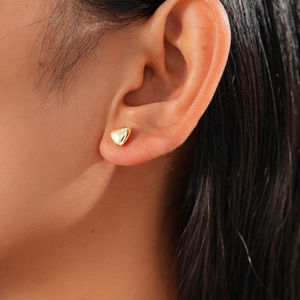 Close-up of a minimalist golden heart-shaped stud earring worn on a model's ear