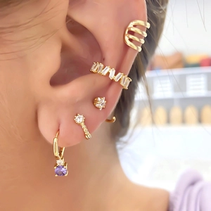 Macro detail of gold earrings set with purple zircon pendant and crystal ear cuffs