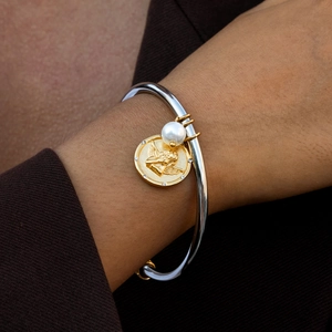 Detail of two-tone steel bangle with white pearl and gold angel relief coin pendant