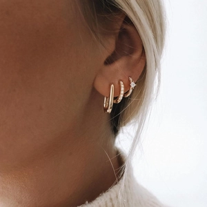 Detailed view of layered 18K gold earrings set with cubic zirconia on model's ear