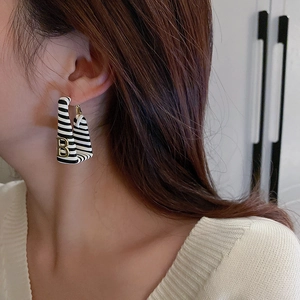 Close-up of model wearing U-shaped black and white striped earring with gold B letter
