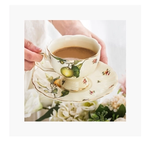 Detailed view of cream ceramic coffee cup with green fruit pattern and gold rim detailing