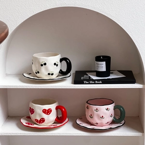 Three ceramic coffee mugs with cherry and heart patterns on a white storage rack
