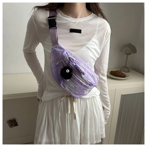 Detail of purple crossbody chest bag with floral embroidery and black plush pompom charm