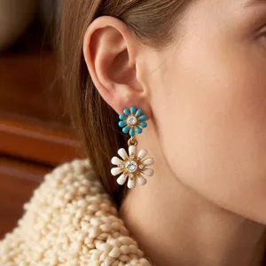 Boucles d'oreilles marguerites dorées élégantes avec émail bleu et cristaux sur un mannequin