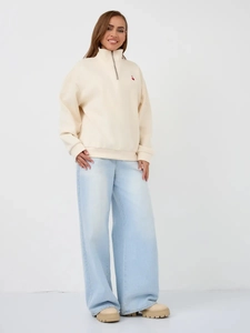 Detail of beige half-zip sweatshirt with red heart embroidery and high-waist denim pants