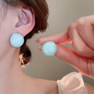 Detailed close-up of light blue marble textured resin stud earrings worn on ear