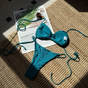 Flachbild eines petrolfarbenen Halter-Bikini-Sets mit seitlichen Bindungen auf Strandmatte